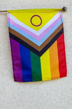 Beyaz duvarda cinsiyetler arası çemberin asılı olduğu Gelişim Gururu Bayrağı. LGBTQ kapsayıcılığı, çeşitlilik ve eşitliğin sembolü.