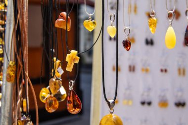 Close-up of various amber pendants and necklaces hanging on display at a market stall, featuring polished stones in different shapes and warm colors.