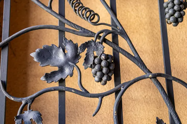 Sarı duvara karşı asma ve yaprak tasarımlı dekoratif dövmeli demir çit yakın plan. Mimarlık ve tasarım konseptleri için sanatsal demircilik işi.