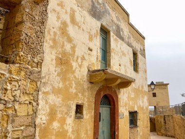 Mdina, Malta 'daki eski sarı bina, mavi ahşap bir kapısı, kemerli girişi ve soluk bir cephesi var. Eskimiş dokular ve yumuşak ışık, zamansız Akdeniz karakterini geliştirir.