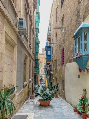 Valletta, Malta 'da dar bir sokak. Geleneksel balkonları, saksıları ve renkli panjurları var. Parlak Akdeniz mimarisi huzurlu bir sokakta.
