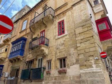 Yol işaretleri olmayan eski kireçtaşı binaların üzerinde renkli geleneksel Malta balkonları. Tarihi bir bölgede şehir manzarası.