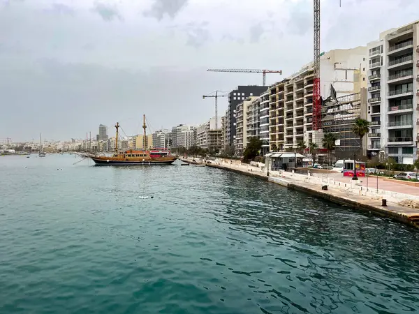 Sliema, Malta 'daki modern binaların yakınında durgun turkuaz sularda geleneksel yelkenli gemi. Güneşli bir günde şehir limanı ve deniz kontrastı.
