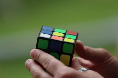 Yumuşak yeşil bir arkaplan üzerinde renkli bir küpü tutan ve döndüren eller.