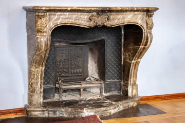 Tarihi bir iç mekânda süslü oymaları ve metal şöminesi olan antik mermer şömine. Şatafatlı klasik tarz, taş şömine ve ahşap zemin.