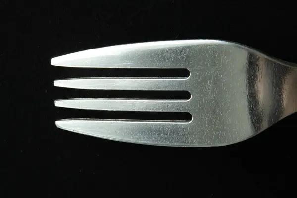 Siyah arka planda gümüş bir metal çatalın makro fotoğrafı. Cilalanmış dokuyu ve basit tasarımı yakından vurgula.