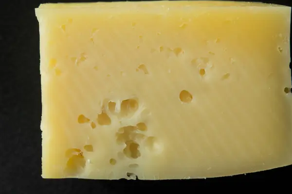 Siyah arka planda izole edilmiş, delikli sarı peynir bloğuna yakın çekim. Yumuşak desenli İsviçre tarzı süt ürünü..