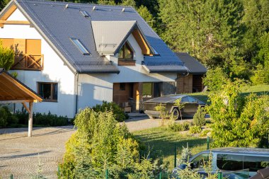 Güneşli bir yaz gününde huzurlu bir kırsal alanda yeşil, ağaçlar ve park edilmiş arabalarla çevrili mavi kiremitli çatılı modern banliyö evi..