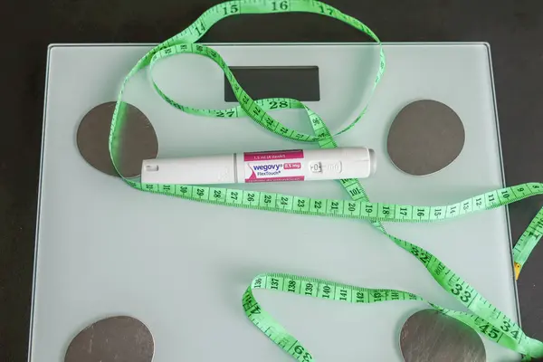 Yılan pençesi. Polonya. 29.07.2025 Wegovy 0.5 mg 'lık enjeksiyon kalemi yeşil bir mezura ile dijital ölçekte yerleştirildi. Kilo kaybı, obezite tedavisi ve vücut ölçümü kavramı.