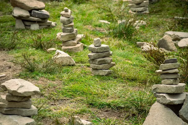 Çimenli zeminde çeşitli boyutlarda çoklu taş cairleri, doğayla dengeyi, barışı ve ahengi sembolize eden sanatsal ve meditasyonsal bir manzara yaratır..