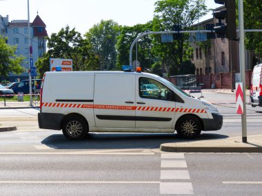 Beyaz minibüs, acil elektrik onarımı için şehrin bir caddesine park edilmiş uyarı çizgileri ve çatı ışıkları olan Elektrik Acil Servisi olarak işaretlenmiş..