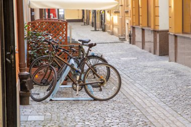 Sıcak güneş ışığı ve geleneksel binaları olan sakin eski bir kasaba sokağında parke taşlı bir caddeye parketmiş bisikletler..