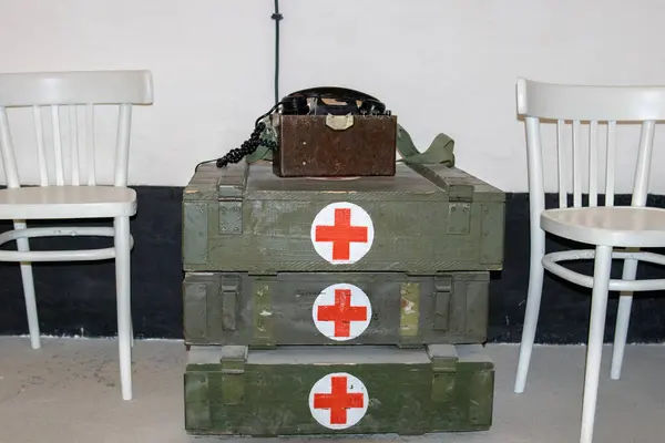 İki beyaz sandalyenin arasında kırmızı haç sembolleri ve klasik saha telefonu olan eski askeri tıbbi kutular. Savaş zamanı sağlık ekipmanları görüntüleme.