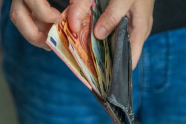 Avro banknotları ve deri bir cüzdan tutan ellerin yakın çekimi. Resim finans, harcama ve günlük para akışını gösteriyor.