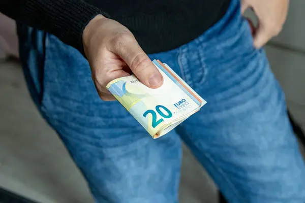 Kot pantolon ve siyah kazak giyen bir adam 20 Euro 'luk banknot yığını tutuyor. Para, tasarruf veya mali işlem kavramı.