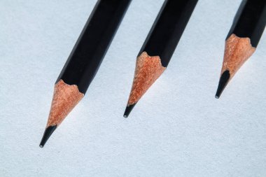 Beyaz kağıt üzerinde üç siyah kaleme yakın çekim. Keskin uçlar ve temiz kompozisyon minimalist bir çalışma alanında hassasiyet ve basitliği vurgular.