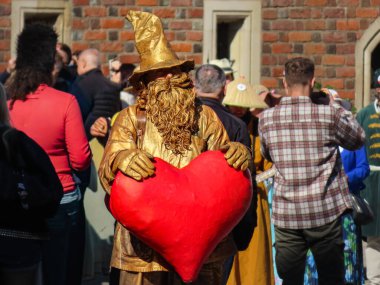 28 Eylül 2025. Yılan pençesi. Polonya. Altın bir büyücü gibi giyinmiş bir sokak sanatçısı, halka açık bir etkinlikte büyük bir kırmızı kalp taşıyor. 28 Eylül 2025. Yılan pençesi. Polonya. Sokak sanatçısı.