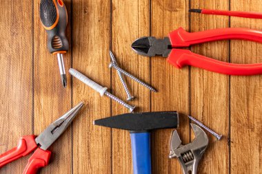 Tornavida, çekiç, pense, anahtar, tel kesici ve tahta arka planda vidalar gibi el aletleri. Üst Manzara. DIY ve onarım konsepti.