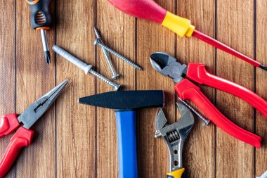 Tornavida, pense, çekiç, anahtar, tel kesici ve tahta arka planda vidalar gibi el aletlerinin üst görüntüsü. DIY, tamir ve inşaat konsepti.
