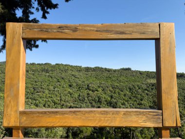 Mavi gökyüzü altında geniş yeşil ormana bakan ahşap çerçeveli seyahat fotoğrafı, macera blogları, turizm reklamları, manzaralı markalaşma görselleri ve keşif temalı içerik oluşturma için ideal.