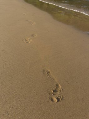 Güzel sahilde ayak izleri. Deniz kıyısındaki ıslak kumda insan ayak izlerine yakın çekim