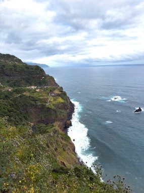 Portekiz, Madeira 'nın kayalık kıyılarında kıyı şeridi ve okyanus dalgalarının dikey görüntüsü. Beyaz sörflü deniz burnu
