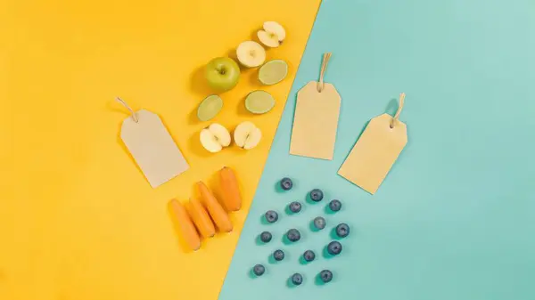 Canlı bir tepeden çekimde elmalar, yaban mersinleri ve buzlu dondurmalar boş etiketlerle parlak sarı ve deniz mavisi bir yüzeye yerleştirilir..