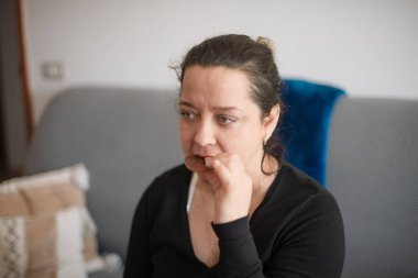 Orta yaşlı bir kadın oturma odasında rahat bir kanepede otururken kurabiye yiyor.