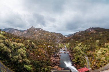 Arka planda bulutlu gökyüzü olan bir kanyona akan barajın panoramik görüntüsü