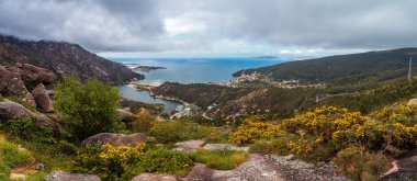 Ezaro 'nun çarpıcı panoramik manzarası, Galiçya, İspanya' da dağlar ve Atlantik Okyanusu arasında yuva yapmış, doğanın güzelliğini ve dramatik bulutlu gökyüzünü gösteren.