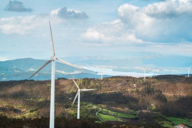 Rüzgâr türbinleri bir dağın tepelerinde, ormanlarda ve bulutlu gökyüzünde temiz enerji üretirler.