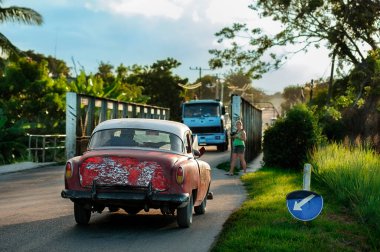 Bir turist köprüden geçen canlı mavi bir kamyonun fotoğraflarını çekerken, Küba 'nın klasik ulaşım cazibesini somutlaştırıyor.