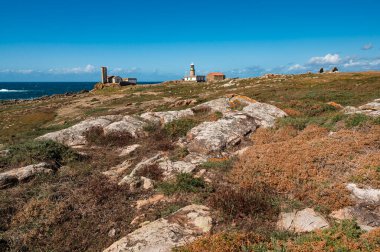 Faro corrubedo deniz feneri kayalıklarda açık mavi bir gökyüzüne karşı duruyor. Costa da Morte 'nin geniş kıyı şeridi. Galiçya. Vahşi Atlantik Okyanusu ve etrafındaki kuru bitki örtüsünün huzurlu bir görüntüsünü sunuyor.