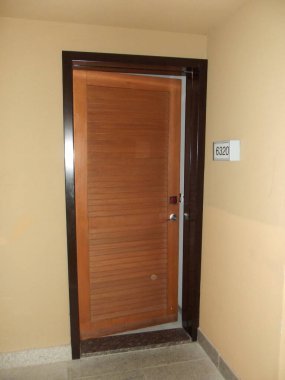 Koyu ahşap çerçeveli, bej duvarlı, yatay çatallı ahşap bir kapı. Kapı kapalı ve küçük yuvarlak bir kapı kolu var. Kapının yanındaki duvarda 6320 numaralı oda var..