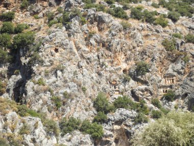Yeşillik ve kayalık arazilerle çevrili engebeli bir yamaçta yuva yapmış antik kaya kesimi mezarlar. Yapılar bitki örtüsüyle kısmen gizlenmiş, doğal ortamlarda tarihsel mimari sergileniyor..
