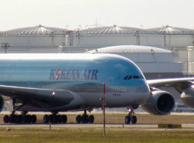 Arka planda büyük depolama tankları olan bir Kore Air Airbus A380 havaalanı pistinde taksicilik yapıyor..