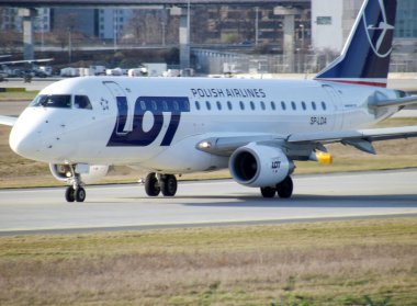 Bir LOT Polonya Havayolları uçağı pistte, kendine özgü giyimi ve tasarımı sergileniyor. Uçak kalkış ya da iniş için hazırlanıyor. Uçağın gövdesi ve kuyruğu net görünüyor..