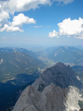 Vadiye bakan bir dağ zirvesinden nefes kesici bir manzara, önplanda engebeli dağ sıraları ve parçalı bulutlu bir gökyüzünün altındaki mesafeye uzanan geniş bir manzara..
