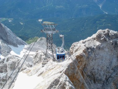 Dik uçurumlar ve aşağıdaki yemyeşil vadilerle çevrili kayalık bir dağın zirvesine tünemiş bir teleferik istasyonu. Sahne, dağlık arazinin engebeli güzelliğini yakalar..