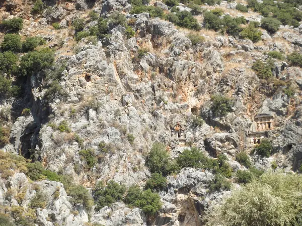 Yeşillik ve kayalık arazilerle çevrili engebeli bir yamaçta yuva yapmış antik kaya kesimi mezarlar. Yapılar bitki örtüsüyle kısmen gizlenmiş, doğal ortamlarda tarihsel mimari sergileniyor..