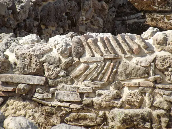 Benzersiz desenleri ve dokuları olan antik taş duvarın yakın çekimi, tarihi bir bölgede taş ve tuğlaların karışımını sergiliyor..