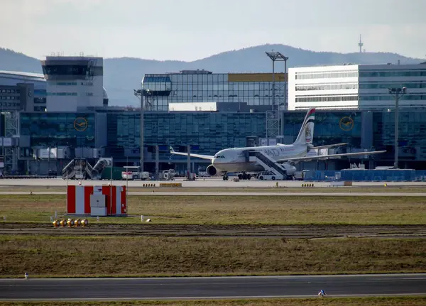 Arka planda modern terminal binaları olan bir havaalanına park edilmiş bir uçak. Sahnede bir kontrol kulesi ve çeşitli havaalanı tesisleri yer alıyor, yoğun bir havacılık ortamı sergileniyor.