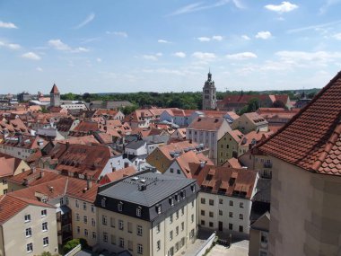 Kırmızı kiremitli çatıları, tarihi binaları ve açık mavi gökyüzü olan panoramik bir kasaba. Sahne, arka planda geleneksel mimarinin ve yeşilliğin cazibesini yakalıyor..