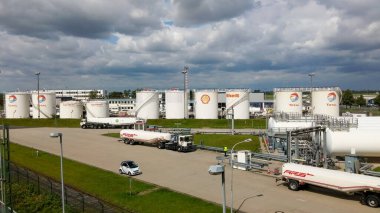 Shell and Total 'dan çok sayıda yakıt depolama tankının bulunduğu büyük bir sanayi bölgesi, yükleme ve boşaltma için yakınlarda kamyonlar park edilmiş. Gökyüzü parçalı bulutlu.
