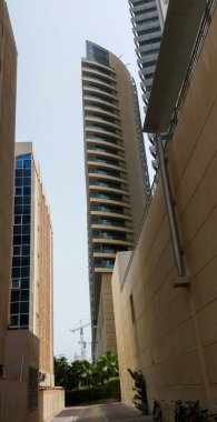 Benzersiz bir spiral tasarımı olan modern bir gökdelen, iki bina arasında yükseliyor. Görüntü, binayı dar bir ara sokaktan yakalıyor. Açık gökyüzüne karşı yüksekliğini ve mimari özelliklerini gösteriyor..