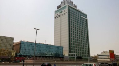 Camdan cepheli ve beyaz dış görünüşlü, kentsel bir alanda kurulu, uzun ve modern bir bina. Binanın birden fazla katı var ve diğer yapı ve araçlarla çevrili..