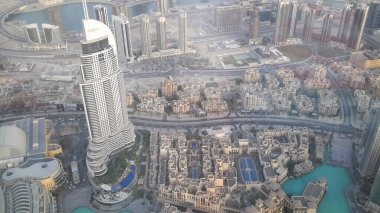 Uzun gökdelenler, dolambaçlı bir yol ve konut ve ticari binaların karışımından oluşan modern bir şehir manzarası. Sahne, şehir manzarasını havuzlar ve yeşilliklerle yakalıyor.