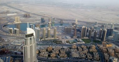 Uzun gökdelenler, dolambaçlı su yolları ve şehir ve çöl manzaralarının karışımından oluşan modern bir şehir manzarası..