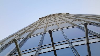 Camdan cepheli ve metal iskeletli modern bir gökdelenin alçak açılı görüntüsü, açık mavi gökyüzüne doğru uzanıyor..