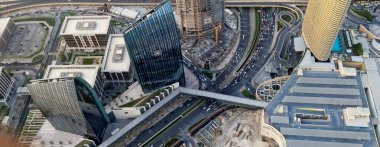 Gökdelenlerin, işlek yolların ve binaları birbirine bağlayan yaya köprüsünün yer aldığı modern şehir manzarası. Sahnede mimari ve şehir hayatının bir karışımı sergileniyor..